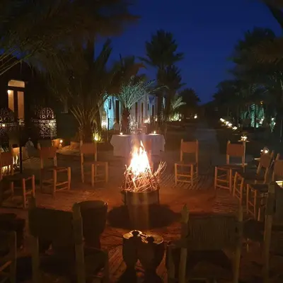 a fire pit with chairs and tables at night at Auberge Sahara Garden in Lac Yasmins