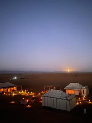 a view of a desert at night with buildings and lights at Desert Luxury Camp Erg Chigaga in El Gouera