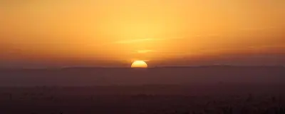 a sunset in the desert with the sun in the horizon at Bivouac Karim Sahara in Zagora