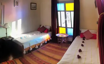 a room with two beds and a table and windows at Le petit Jardin in Demnat