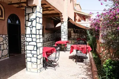 an outdoor patio with tables and chairs with red table cloth at La Rose De Sable in Aït Ben Haddou