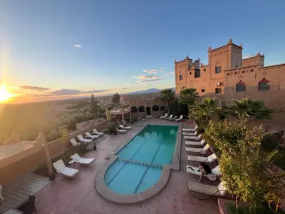 an outdoor swimming pool with lounge chairs and a building at Kasbah Ait BenHadda in Skoura