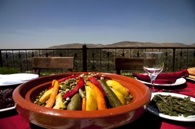 a bowl of vegetables on a table with a glass of wine at Kasbah Illy in Demnat