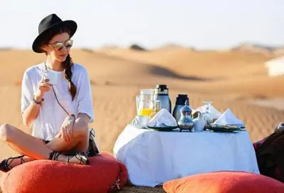 a woman sitting at a table in the desert at Camp Sahara Majestic in Mhamid