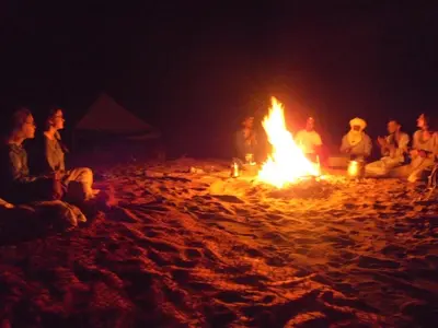 a group of people sitting around a fire on the beach at Desert Atmosphere M'Hamid in Mhamid