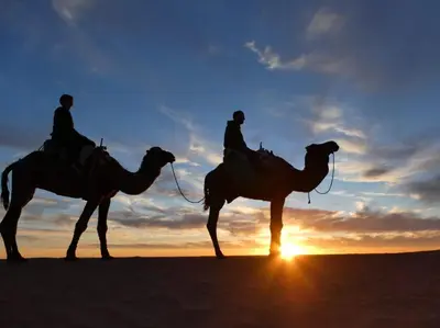 two people riding camels in the desert at sunset at Desert Atmosphere M'Hamid in Mhamid