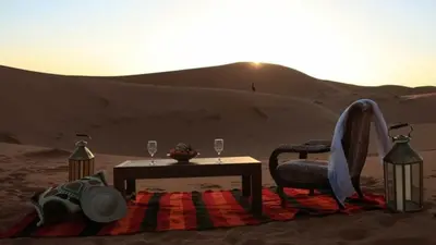 a table and chair in the desert with a table and glasses at Erg Chebbi Luxury Camp in Merzouga
