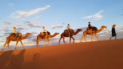 a group of people riding on camels in the desert at Erg Chebbi Luxury Camp in Merzouga