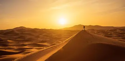 a person standing on a desert road in the sunset at Erg Chebbi Luxury Camp in Merzouga