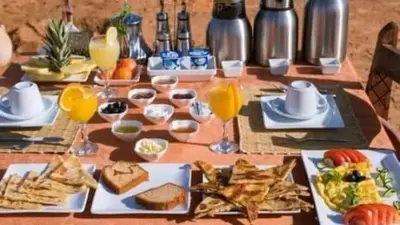 a table with plates of food and glasses of orange juice at Erg Chebbi Luxury Camp in Merzouga