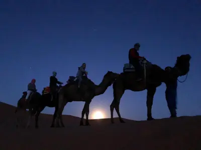 a group of people riding on camels in the desert at Merzouga Camp and Hostel in Merzouga