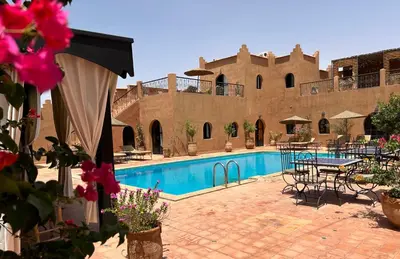 a swimming pool with tables and chairs next to a building at Riad Dar Bergui in Ouarzazate