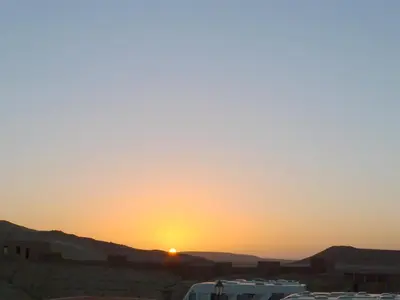 a sunset in the desert with cars parked at Maison d'Hôtes Nouflla in Aït Ben Haddou