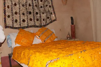 a bed with an orange blanket and pillows on it at Kasbah Dar Dmana in Skoura