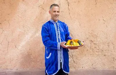 a man holding a bowl of fruit in front of a wall at Ecolodge La Palmeraie in Ouarzazate