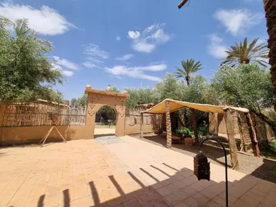 a patio with an arch and a fence and trees at Eco-Ferme Tamalait Skoura in Skoura