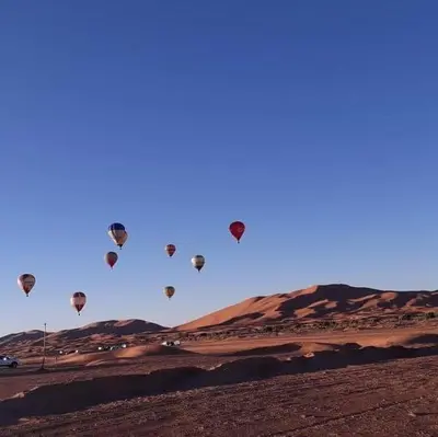 a bunch of hot air balloons flying in the sky at sand rose luxury camp in Merzouga
