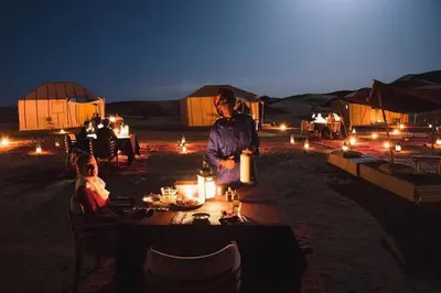 a woman sitting at a table in the desert at night at sand rose luxury camp in Merzouga