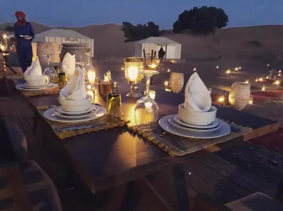 a wooden table with plates and napkins on it with candles at sand rose luxury camp in Merzouga