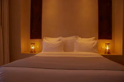a bedroom with a bed with white pillows and two lights at Chez Ichou in Aït Idaïr