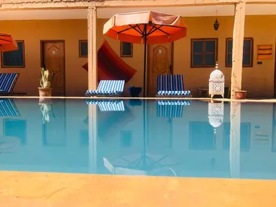 a swimming pool with two chairs and an umbrella at Riad Hotel Les Flamants in Merzouga