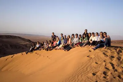 a group of people sitting on top of a sand dune at bassou luxury camp in Merzouga