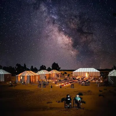two people sitting in front of tents under a starry sky at bassou luxury camp in Merzouga