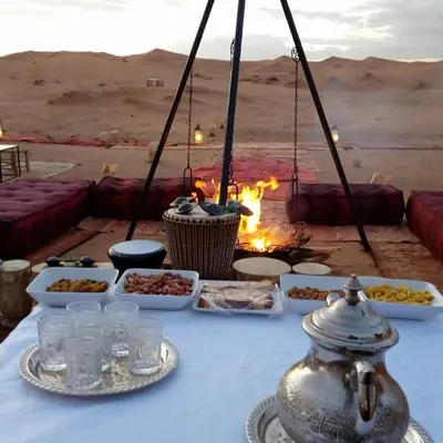 a table with food and a fire in the desert at bassou luxury camp in Merzouga