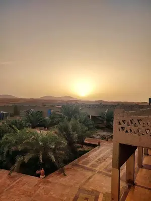 a sunset over the desert with a sign in the foreground at Sahara Sands Hotel in Merzouga