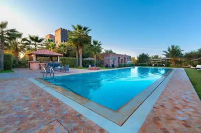 a large swimming pool in a yard with palm trees at La Citadelle Marrakech in Marrakech