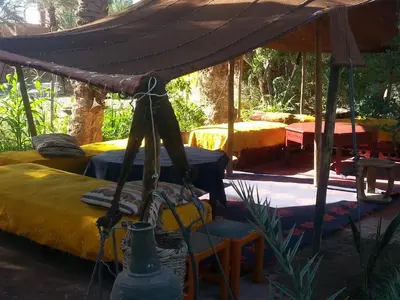a tent with two beds and a table and chairs at Auberge jnane dar diafa se trouve au centre de tamegrouteface de la bibiotheque in Tamegroute