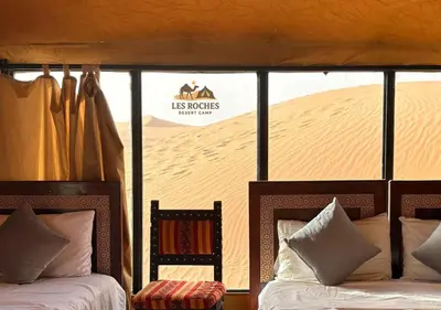 a bedroom with two beds in front of a sand dune at Les Roches Desert Camp in Merzouga