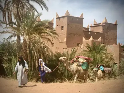 two people walking a camel in front of a castle at Hotel Carrefour des Nomades in Mhamid