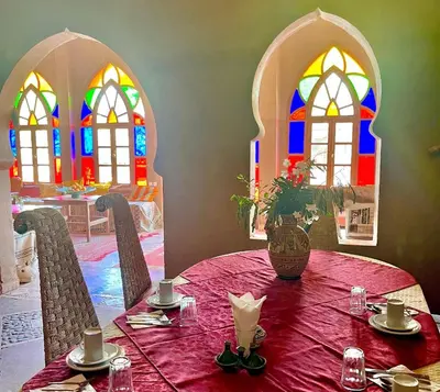 a dining room with a table and stained glass windows at Hotel Carrefour des Nomades in Mhamid