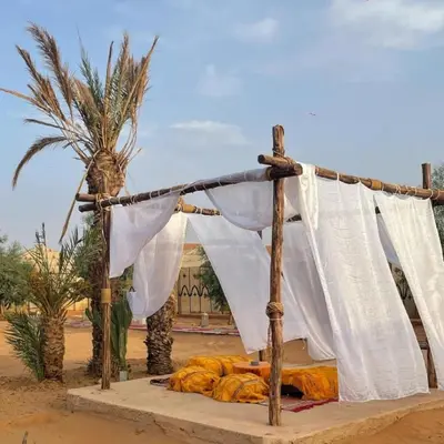 a bed in the middle of a desert with a palm tree at Royal Luxury Cafe Du Sud in Merzouga
