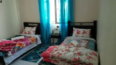 a bedroom with two beds and a window with blue curtains at Hotel Nice 06 in Midelt