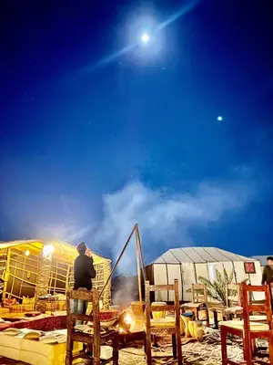 a man sitting on a chair in front of a table at Africa Luxury Camps - Merzouga Premium Camp in Merzouga