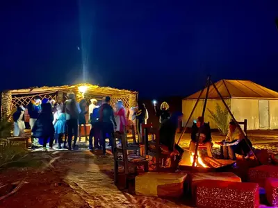 a group of people standing around a tent at night at Africa Luxury Camps - Merzouga Premium Camp in Merzouga
