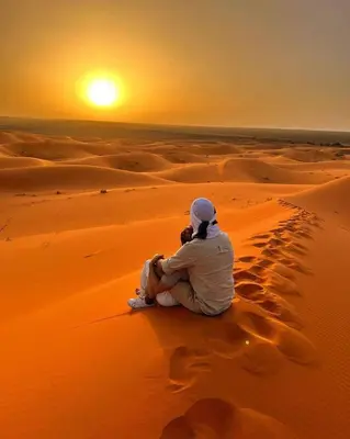 a man sitting in the desert watching the sunset at Deep Desert Camp in Merzouga