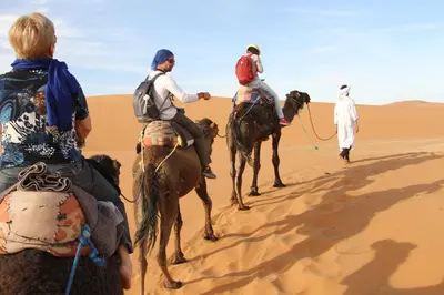 a group of people riding camels in the desert at Chez zakaria luxury camp merzouga in Merzouga