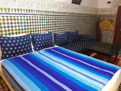 a bed with blue and white striped sheets and a table at Riad El Bacha in Fès