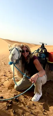 a woman posing with a camel in the desert at Sahara Sunset Camp M'hamid in Mhamid