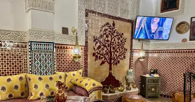 a living room with a couch and a tv on a wall at Riad Le Petit Patrimoine De Fés in Fès