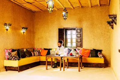 a man sitting on a couch with a laptop on a table at Riad Caravasar in Merzouga
