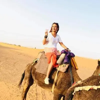 a woman riding on the back of a camel in the desert at L'homme Du Désert A Merzouga in Merzouga