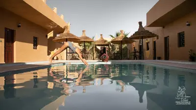 a woman is jumping into a swimming pool at L'homme Du Désert A Merzouga in Merzouga