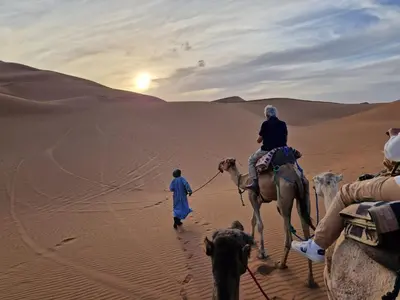 a group of people riding camels in the desert at Camp Desert Bivouac Chegaga in El Gouera