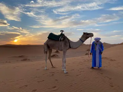 a man standing in the desert with a camel at Desert Bivouac Mhamid in Mhamid
