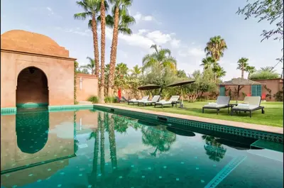 a swimming pool with chairs and palm trees next to a house at Villa Magtafa in Marrakech