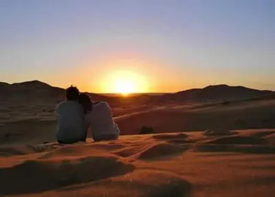 a couple sitting in the desert watching the sunset at Sultan Luxury Camp in Merzouga